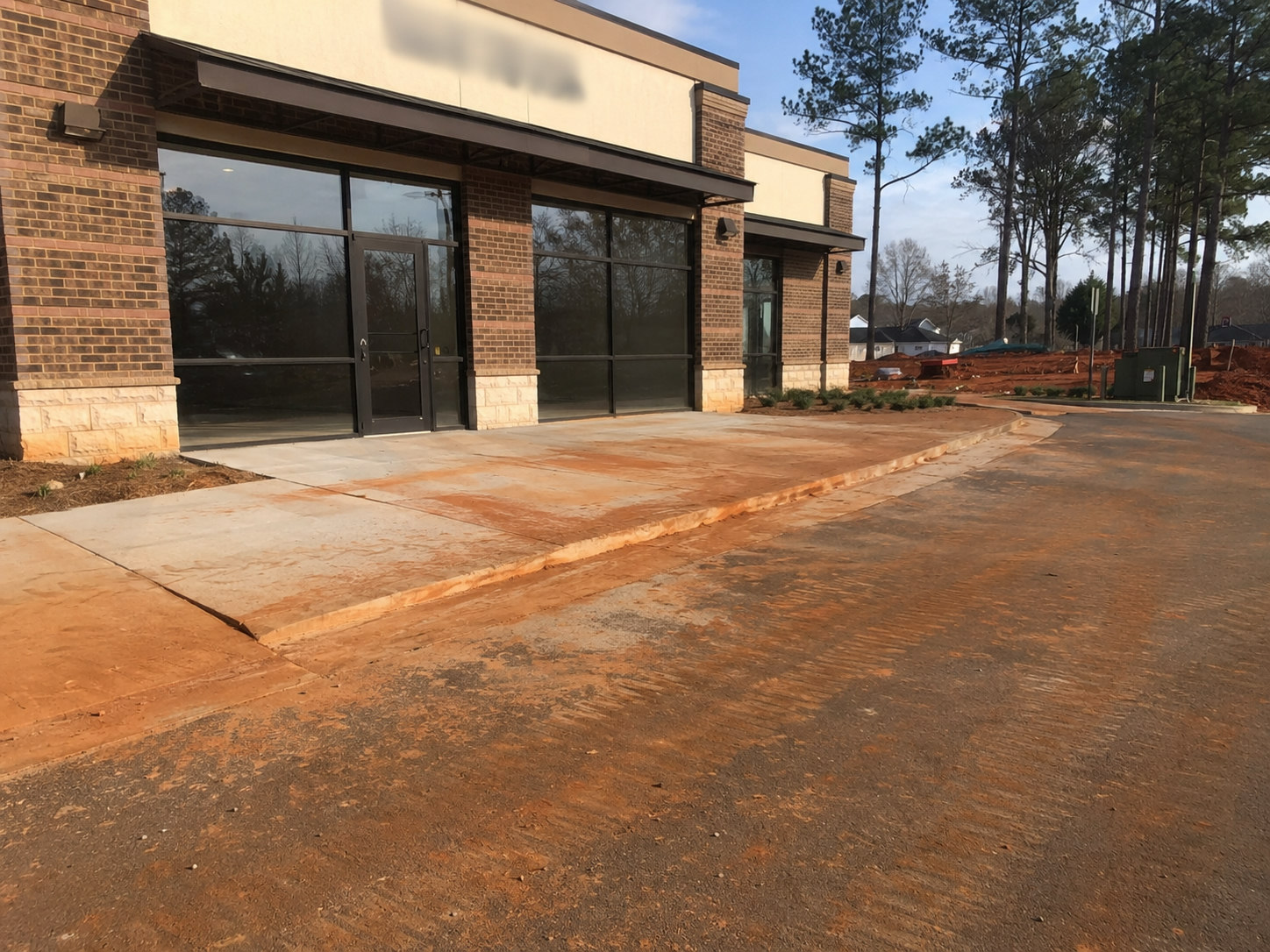Storefront entry walkway and drive lane coated in tracked-in Georgia red clay from nearby construction