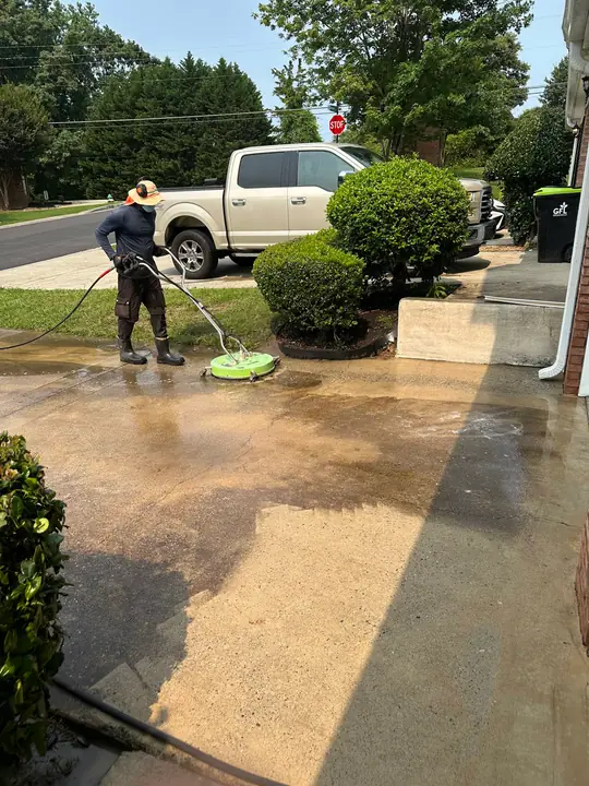 Pressure washing in progress showing a clear contrast between cleaned and stained concrete driveway sections.