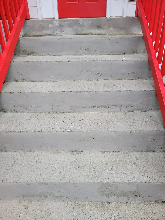 Bright concrete entry steps after pressure washing between red-painted railings.