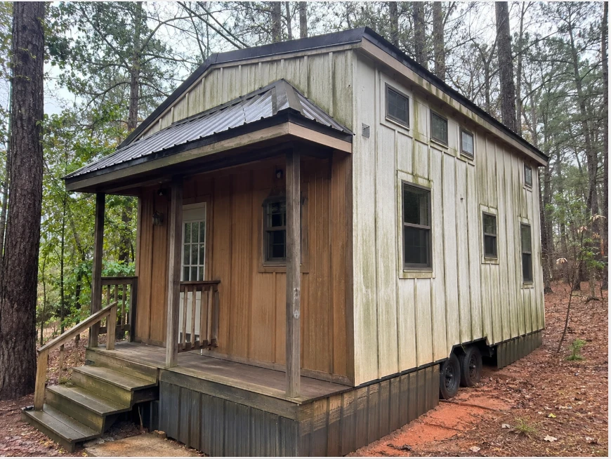 Small Georgia tiny home on a wooded lot with pollen film, mildew streaking, and dirt on the siding and skirting